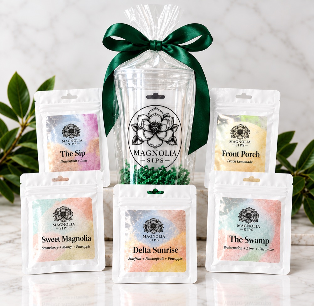 Magnolia Sips gift cup tied with a green ribbon, surrounded by packets of Sweet Magnolia, Delta Sunrise, The Sip, The Swamp, and Front Porch.
